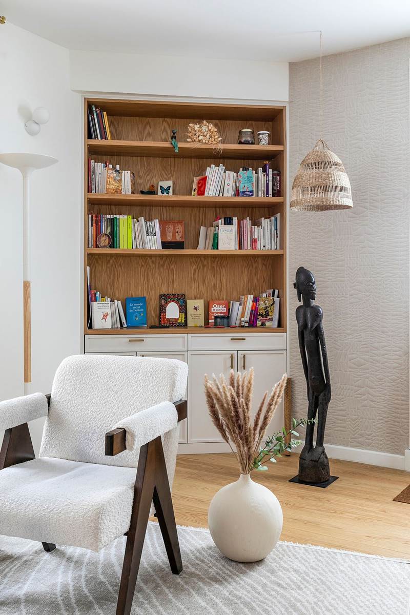 La bibliothèque en chêne du cabinet garnie de livres de psychothérapie, près d'un fauteuil blanc et d'un vase d'herbes sèches.