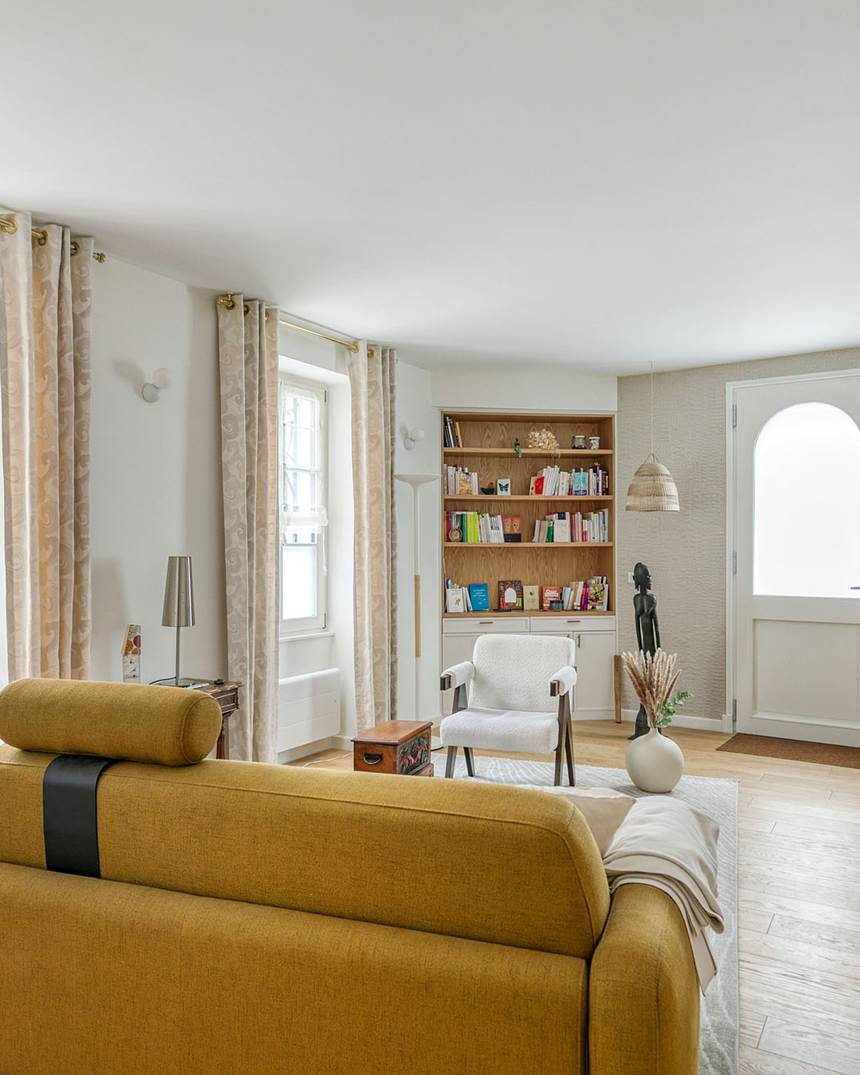 Le canapé moutarde du cabinet vu de dos, tourné vers le fauteuil blanc ; au fond la bibliothèque en chêne et la porte d'entrée.