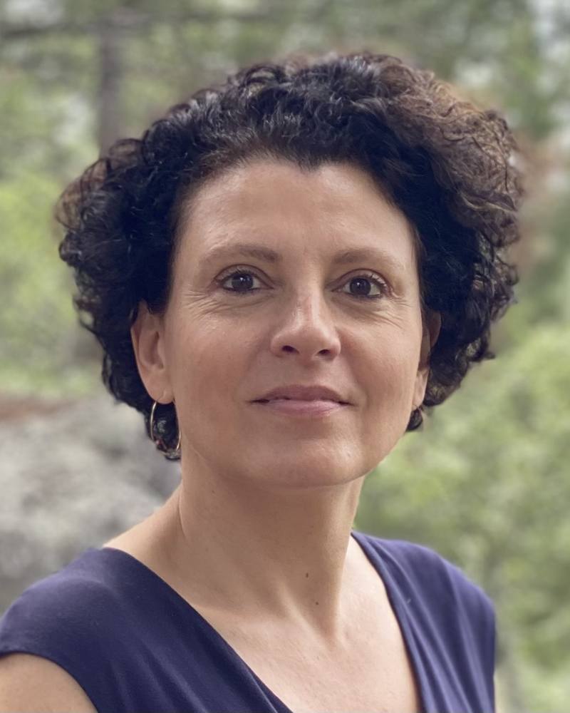 Portrait d'Emmanuelle Galy, Gestalt-thérapeute à Paris 14e, souriante devant un feuillage.